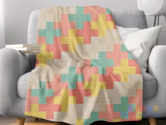 The Modern Kawaii Crosses crochet blanket draped over the arm of a contemporary grey sofa. This colorful C2C design by Ariana Wimsett of Magic Yarn Pixels adds a pop of pastel color to the room.
