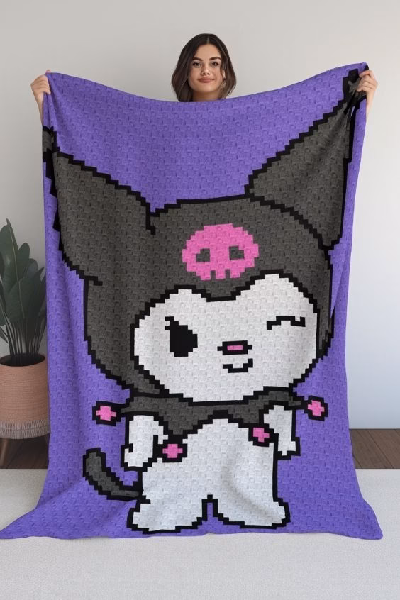 A woman holding up a large crocheted corner-to-corner blanket featuring the character Kuromi on a bright purple background, featured in a crochet roundup from https://magicyarnpixels.com/.