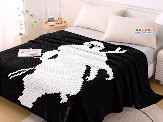 A black and white C2C crochet blanket featuring a pixel art silhouette of The Mandalorian laid flat on a bed in a brightly lit bedroom. Original design by Ariana of MagicYarnPixels.