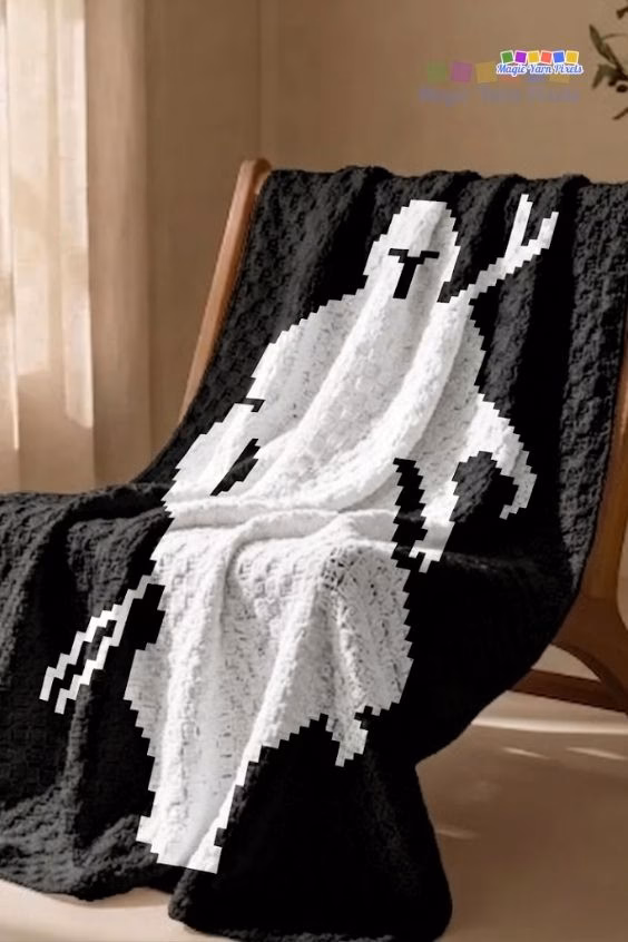 A black and white C2C crochet blanket featuring a pixel art silhouette of The Mandalorian draped over a wooden armchair. Original design by Ariana of MagicYarnPixels.