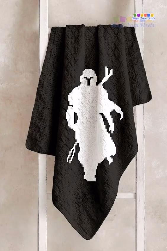 A black and white C2C crochet blanket showing a pixel art silhouette of The Mandalorian displayed on a wooden blanket ladder. Original design by Ariana of MagicYarnPixels.
