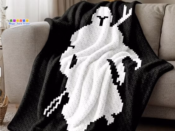 A black and white C2C crochet blanket featuring a pixel art silhouette of The Mandalorian displayed across a gray living room couch. Original design by Ariana of MagicYarnPixels.