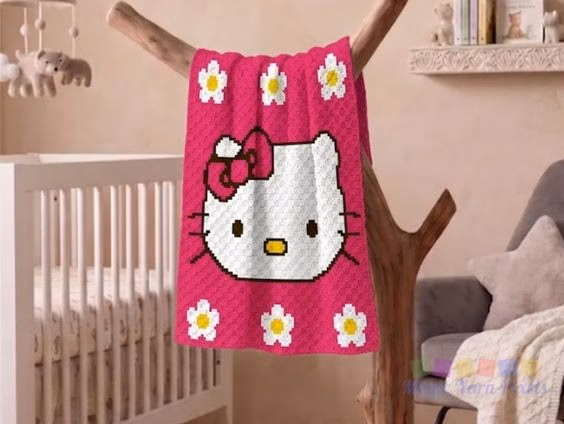 Cute Hello Kitty C2C crochet blanket hanging over a decorative wooden branch in a nursery room setting, displaying a white Hello Kitty face with a dark pink bow on a hot pink background with white and yellow flowers. Original design created by Ariana Wimsett at MagicYarnPixels.com