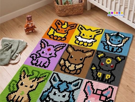A corner-to-corner (C2C) crochet blanket laid flat on a light wood floor in a cozy nursery setting. The blanket features a 3x3 pixel art grid displaying nine Pok&eacute;mon from the Eevee family tree, including Flareon, Jolteon, Vaporeon, Espeon, Eevee, Umbreon, Leafeon, Glaceon, and Sylveon. In the background, a woven basket, a wooden toy fox stacker, and the corner of a white crib are visible. A small "Magic Yarn Pixels" logo is positioned in the upper right. Original design by Ariana of MagicYarnPixels.