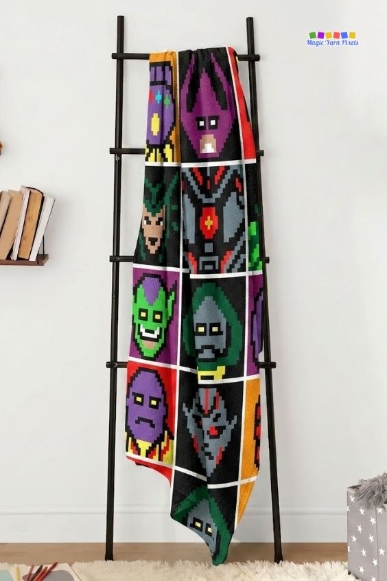 A corner-to-corner (C2C) crochet blanket with a twelve-panel grid layout of colorful pixel art blocks showing different Avengers villains, draped vertically over a dark metal display ladder against a plain white wall. Original design by Ariana of MagicYarnPixels.
