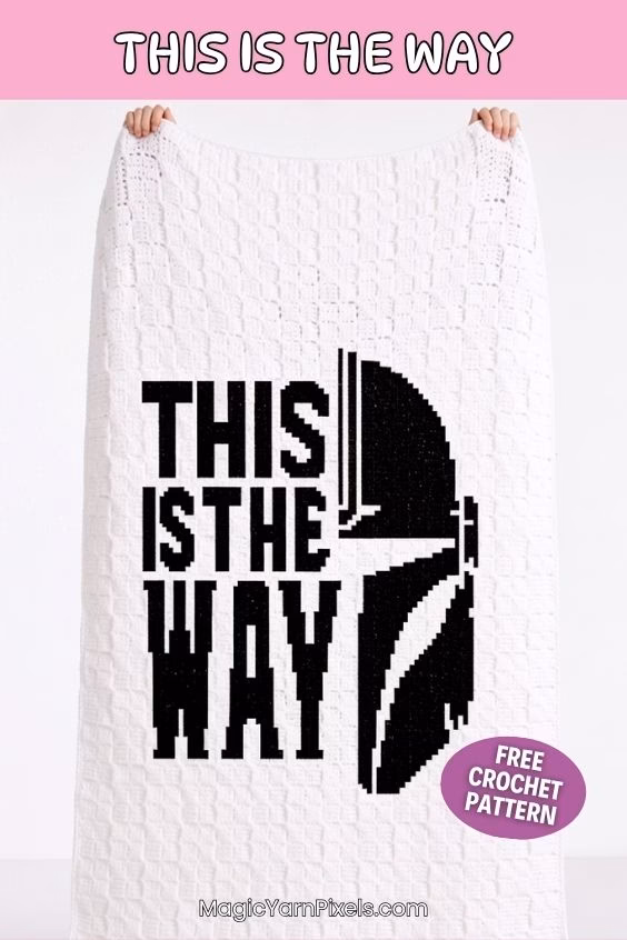 Two hands holding up a large white crochet blanket against a plain background. The blanket features a black pixel design of a Mandalorian helmet and the words "THIS IS THE WAY". A purple sticker says "FREE CROCHET PATTERN". Original design by Ariana of MagicYarnPixels.