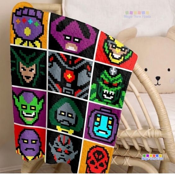A corner-to-corner (C2C) crochet blanket draped over a light-colored wicker chair next to a teddy bear cushion. The blanket features a grid of colorful pixel art style blocks depicting various Avengers villains, including the Infinity Gauntlet, Galactus, and Loki. Original design by Ariana of MagicYarnPixels.