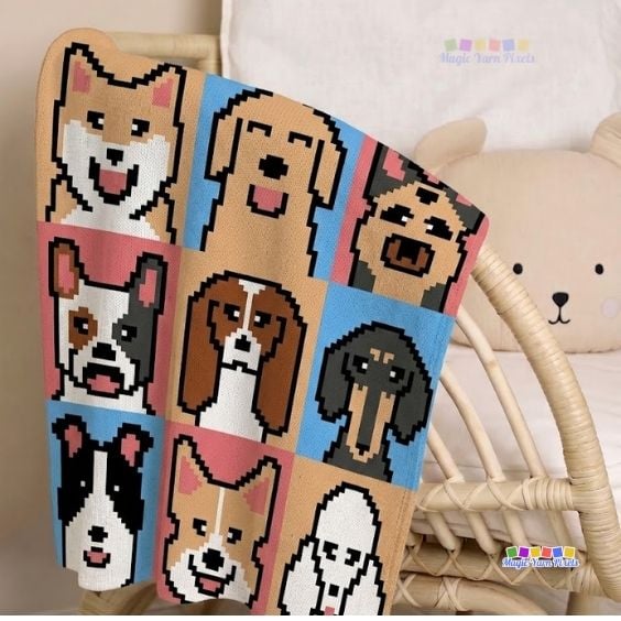 A close-up shot of a textured crochet blanket hanging over the side of a white wicker crib next to a plush bear pillow. The colorful corner-to-corner blanket displays pixelated portraits of various dog breeds on colorful square backgrounds. A small "Magic Yarn Pixels" logo is positioned in the bottom right corner. Original design by Ariana of MagicYarnPixels.