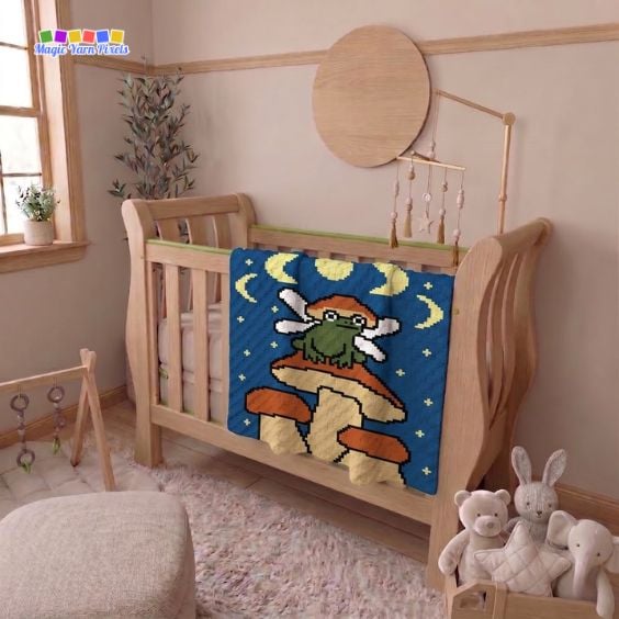 Fairy Frog crochet blanket draped over a nursery crib with a fairy frog, mushrooms, moon, and stars. Original design by Ariana of MagicYarnPixels.