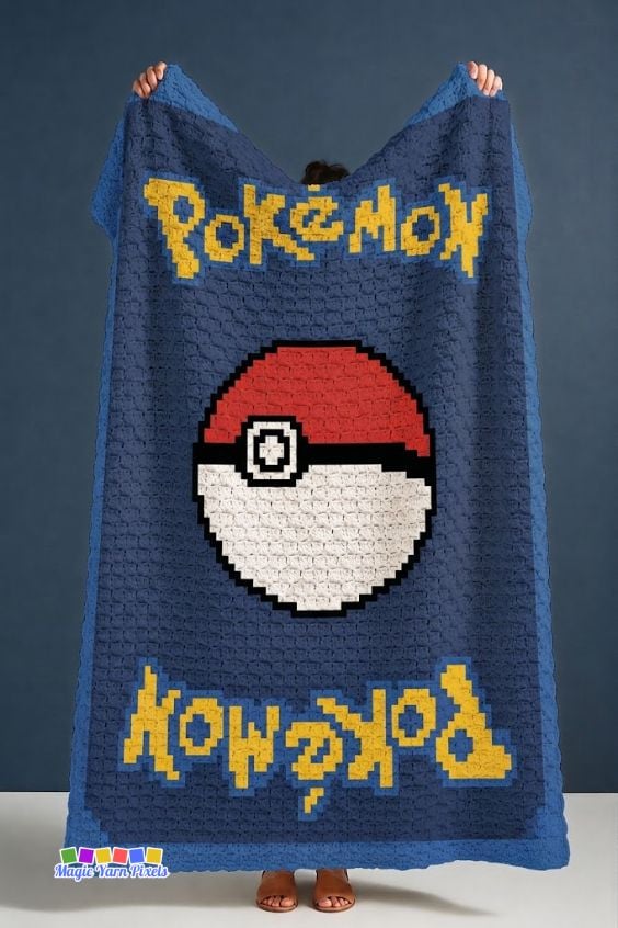Large C2C crochet blanket held up for display, featuring a Pokémon card-inspired design with a centered Poké Ball, yellow pixel lettering, and a blue border. Original design by Ariana of MagicYarnPixels.