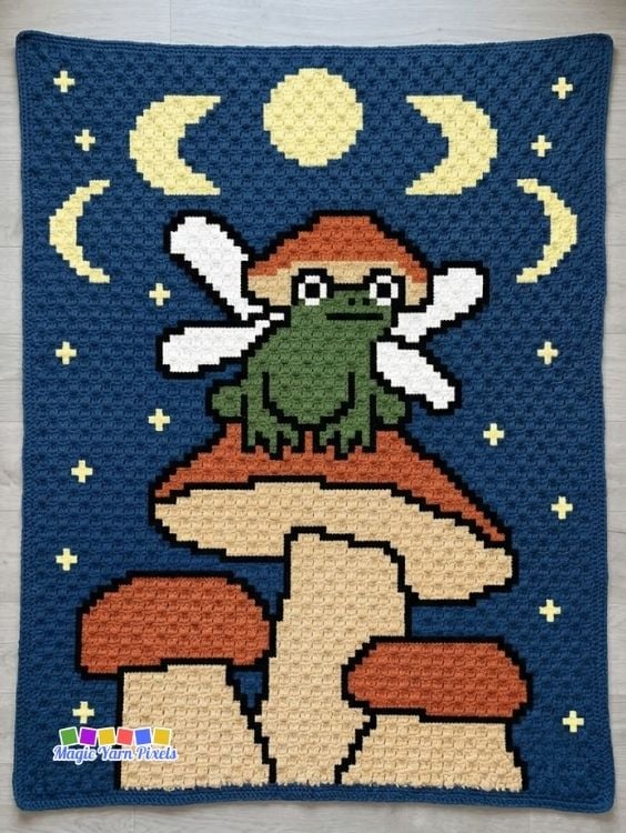 Fairy Frog C2C crochet blanket with a green fairy frog, mushrooms, moon, and stars displayed flat. Original design by Ariana of MagicYarnPixels.