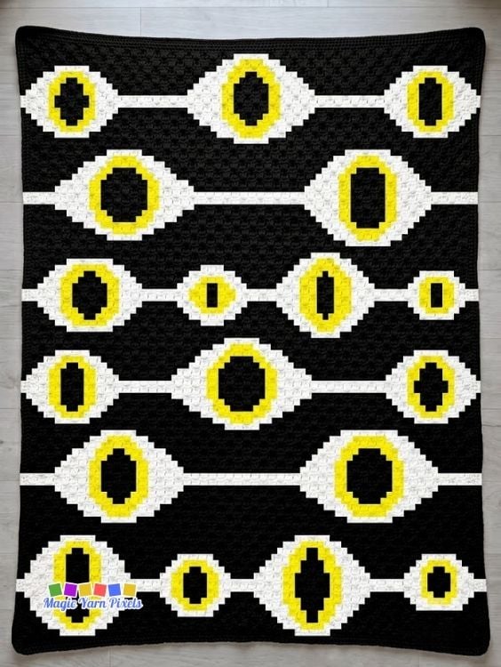 Full view of the finished Witchcraft Evil Eye C2C crochet blanket with repeating evil eye pattern in black, white, and yellow. Original design by Ariana of MagicYarnPixels.