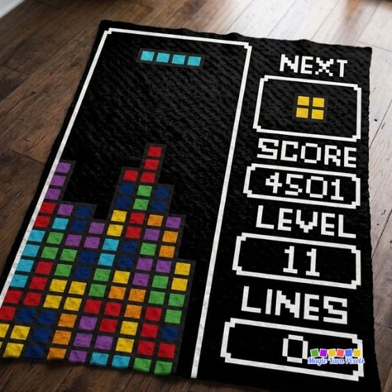 Finished Retro Arcade Blocks C2C crochet blanket with colorful pixel blocks, game-style score display, and black border, photographed on a dark wooden floor. Original design by Ariana of MagicYarnPixels.