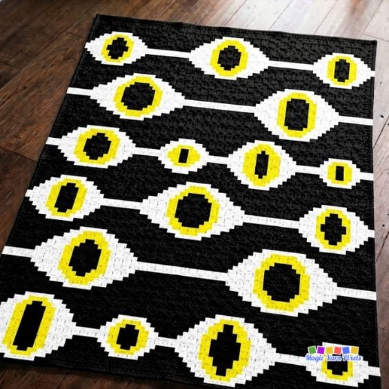 Pixel graph for the Witchcraft Evil Eye C2C blanket showing repeating evil eye motifs in black, white, and yellow. Free evil eye crochet pattern. Original design by Ariana of MagicYarnPixels.