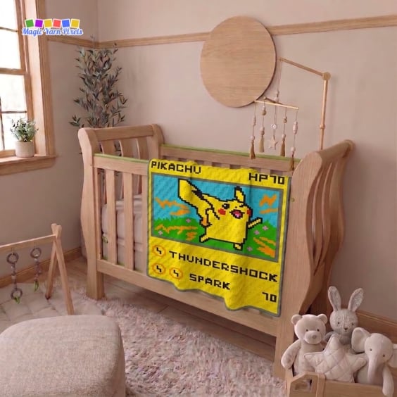 A finished Pikachu Pok&eacute;mon Card C2C crochet blanket hangs over the side of a wooden crib in a nursery with neutral d&eacute;cor, showing Pikachu, "HP70," lightning effects, and the attacks "THUNDERSHOCK" and "SPARK" on a Pok&eacute;mon-style trading card design. Original design by Ariana of MagicYarnPixels.
