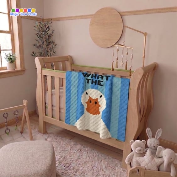 C2C crochet blanket draped over the side of a wooden crib in a nursery. The blanket features a white duck with an orange bill, blue striped columns, and the words "WHAT THE" above the duck. Plush toys and nursery decor surround the crib. Original design by Ariana of MagicYarnPixels.