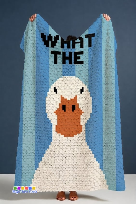 Person holding a completed C2C crochet blanket in front of a blue backdrop. The blanket shows a white duck with an orange bill on blue striped columns with the words "WHAT THE" across the top in bold black letters. Original design by Ariana of MagicYarnPixels.